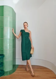 Model wearing a dark green midi dress and strappy sandals standing beside a curved green tiled pillar