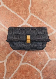 Black woven straw clutch bag with gold clasp resting on a patterned terracotta stone surface