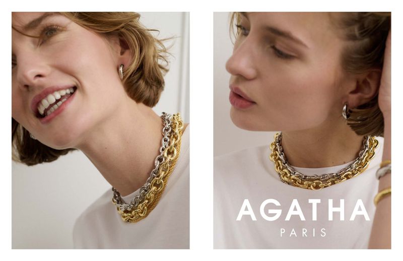 Close-up of a smiling woman wearing a gold and silver chain necklace, silver hoop earrings, and a white top in a studio setting.