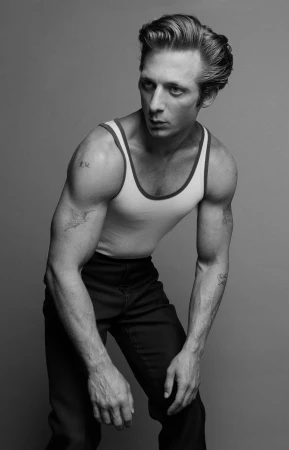 Monochrome portrait of a muscular adult male in a white tank top and dark pants, gazing away against a neutral grey background.
