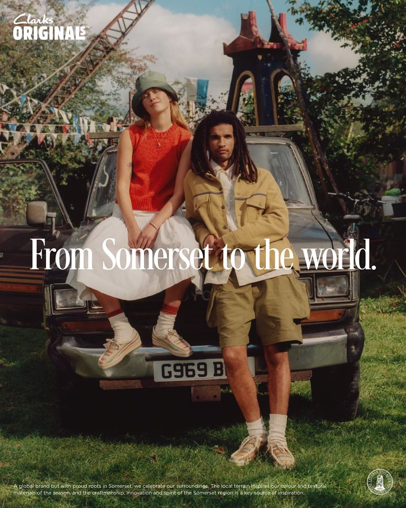 Editorial image of a fair-skinned woman and a dark-skinned man posing next to an old car in a grassy field for a Clarks Originals ad.