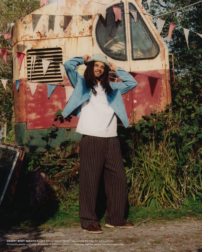 A man in casual wear stands in front of a rustic trailer adorned with bunting, creating an inviting, outdoor fashion shot.