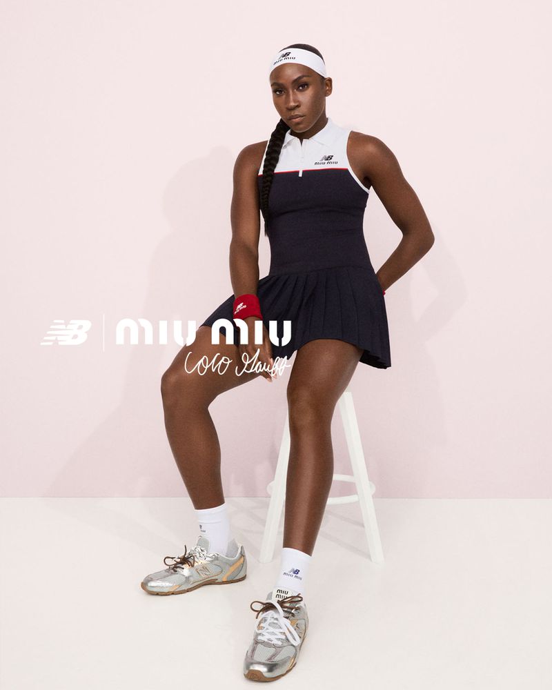 Coco Gauff poses in a navy tennis dress with a white top and matching headband in a studio, wearing metallic sneakers. Logos visible.
