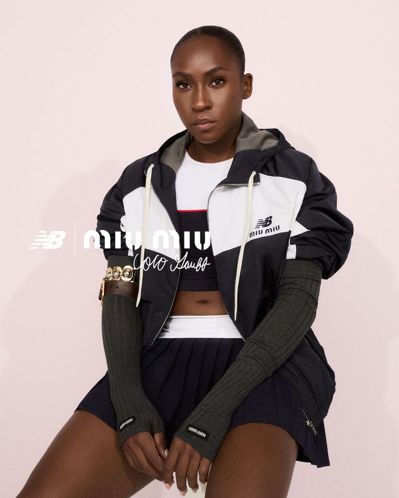 Coco Gauff poses in athletic wear by New Balance and Miu Miu, wearing a navy jacket, pleated skirt, and arm warmers against a pink backdrop.