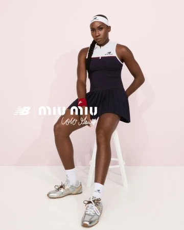 Coco Gauff seated on a white stool wearing a navy pleated tennis dress and silver sneakers against a pale backdrop