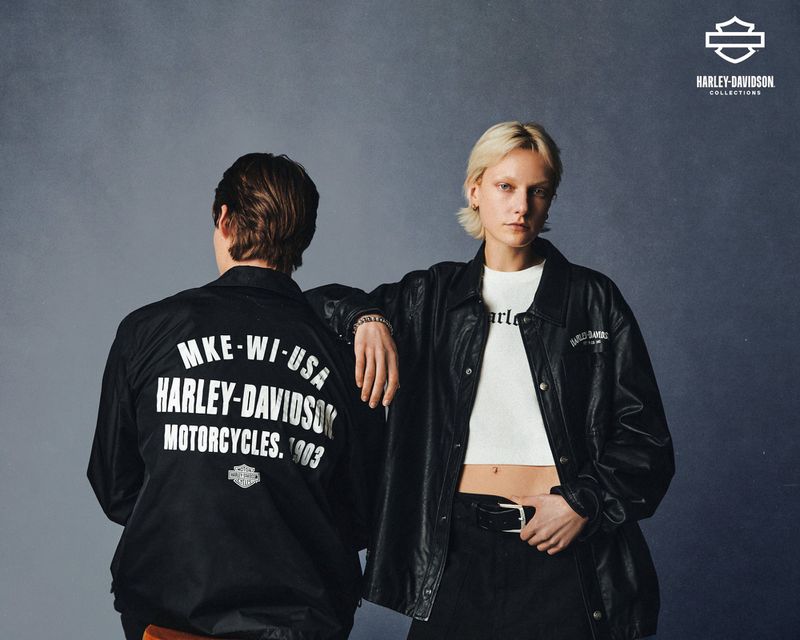 Two people wearing Harley-Davidson jackets stand in front of a gray backdrop in a fashion shot, showcasing motorcycle-themed apparel.