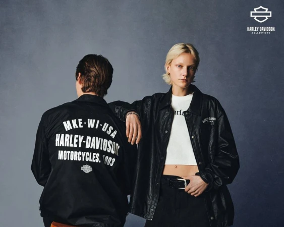 Two people wearing Harley-Davidson jackets stand in front of a gray backdrop in a fashion shot, showcasing motorcycle-themed apparel.