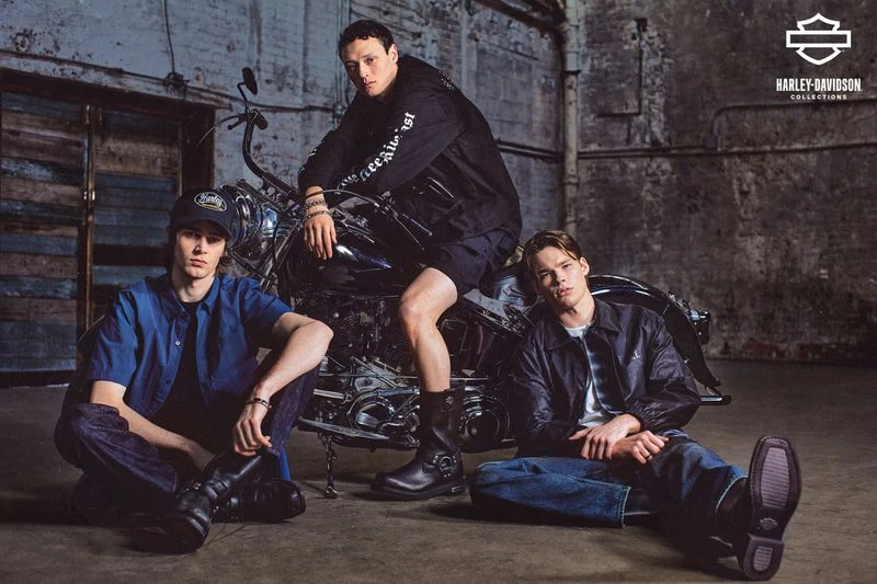 Three adult males showcase Harley-Davidson apparel, seated and posed around a motorcycle in a studio with industrial-style walls and flooring.