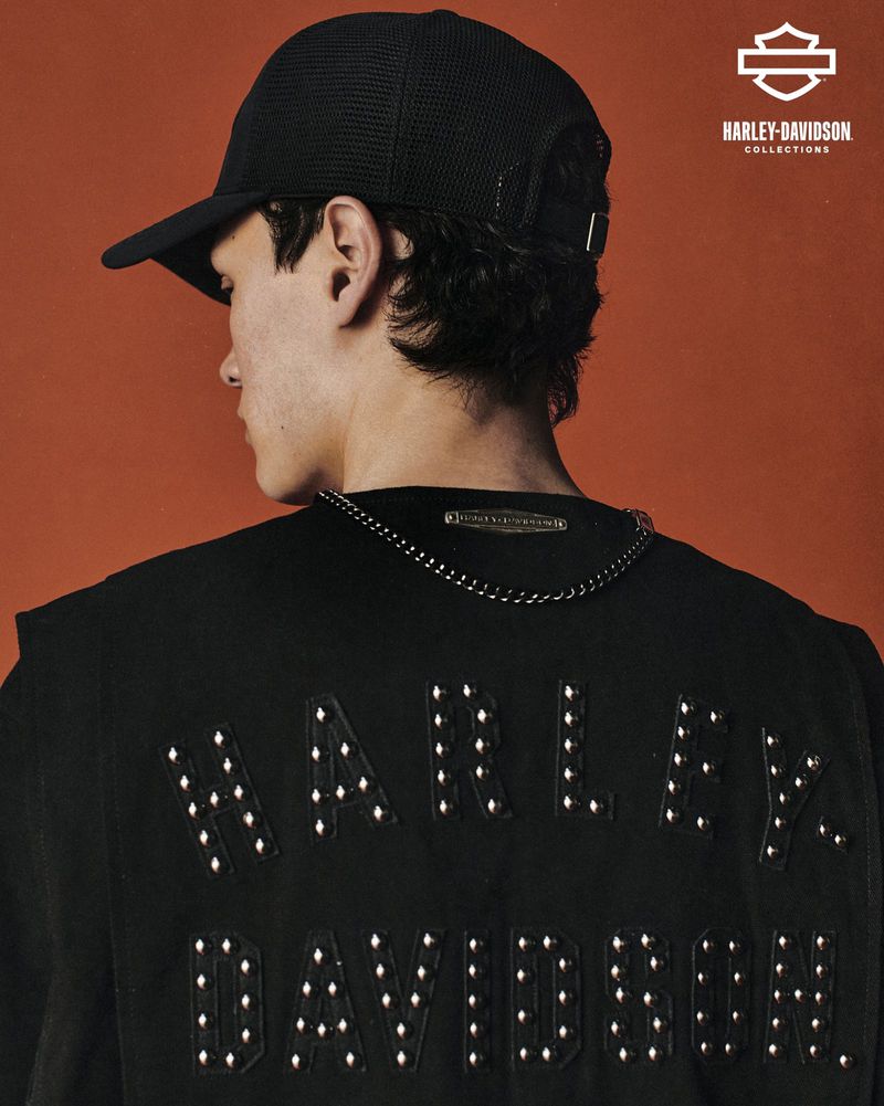 Person with black baseball cap and black shirt with the text 'HARLEY-DAVIDSON' studded on the back against an orange backdrop.