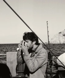 Man wearing a jacket holding a vintage camera on a boat at sea for Falconeri Cruise Collection