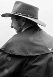 Monochrome close-up of a smiling man in profile wearing a wide-brimmed felt hat and a dark canvas coat