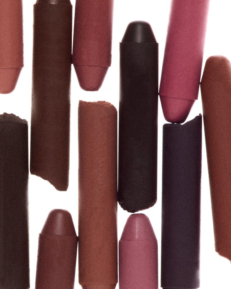 Close-up of assorted lipsticks and cosmetic pencils in shades of brown, mauve, and red-violet on a white surface.