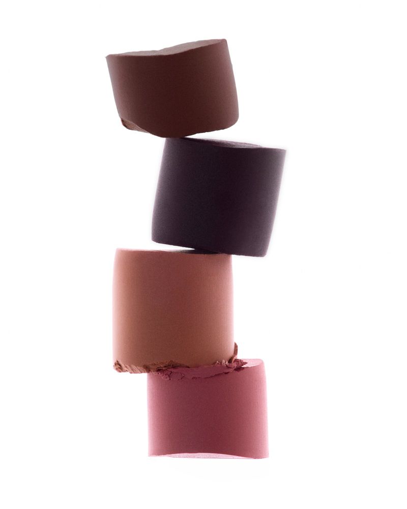 Four cylindrical makeup products stacked on top of one another in the center against a white background in a vertical, studio shot.