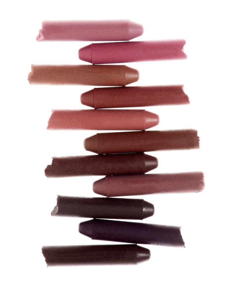 Stack of colorful lipstick crayons of various shades of pink, mauve, and brown on a white background in a studio shot.