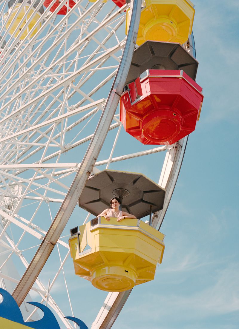 Low angle view of a woman riding a colorful ferris wheel against a clear blue sky during the daytime in an outdoor setting.