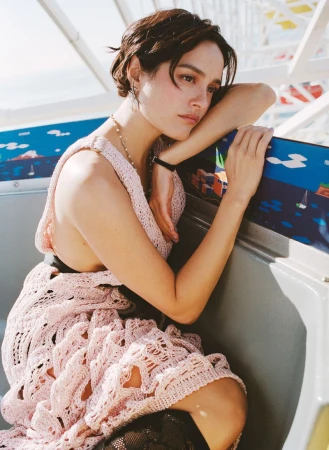 Chase Sui Wonders in a pink crochet dress leaning against a white railing with a painted amusement panel in the background.