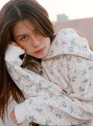 Young woman with freckles wearing a printed white zip-up hoodie, photographed outdoors by Daria Kobayashi Ritch for Ashley Williams SS25.