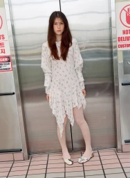 Model wearing a white floral print dress and white tights standing in front of closed metallic elevator doors for Ashley Williams SS25.