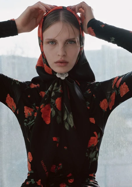 A fashion shot showcases a woman in a black, rose-patterned dress and headscarf, gazing intensely at the camera against a bright window.