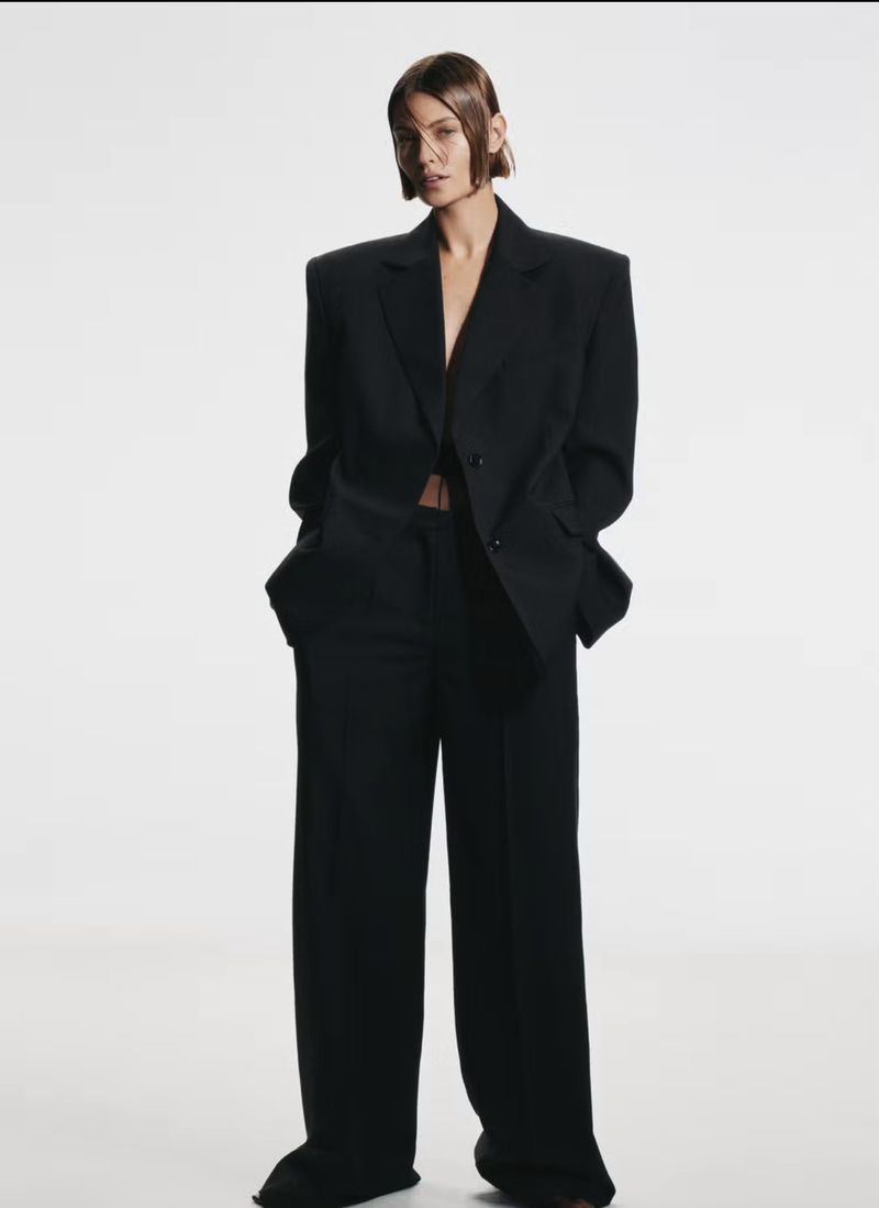 Stylish woman in black blazer and pants posing in photo studio. Fashion editorial shot with clean background.