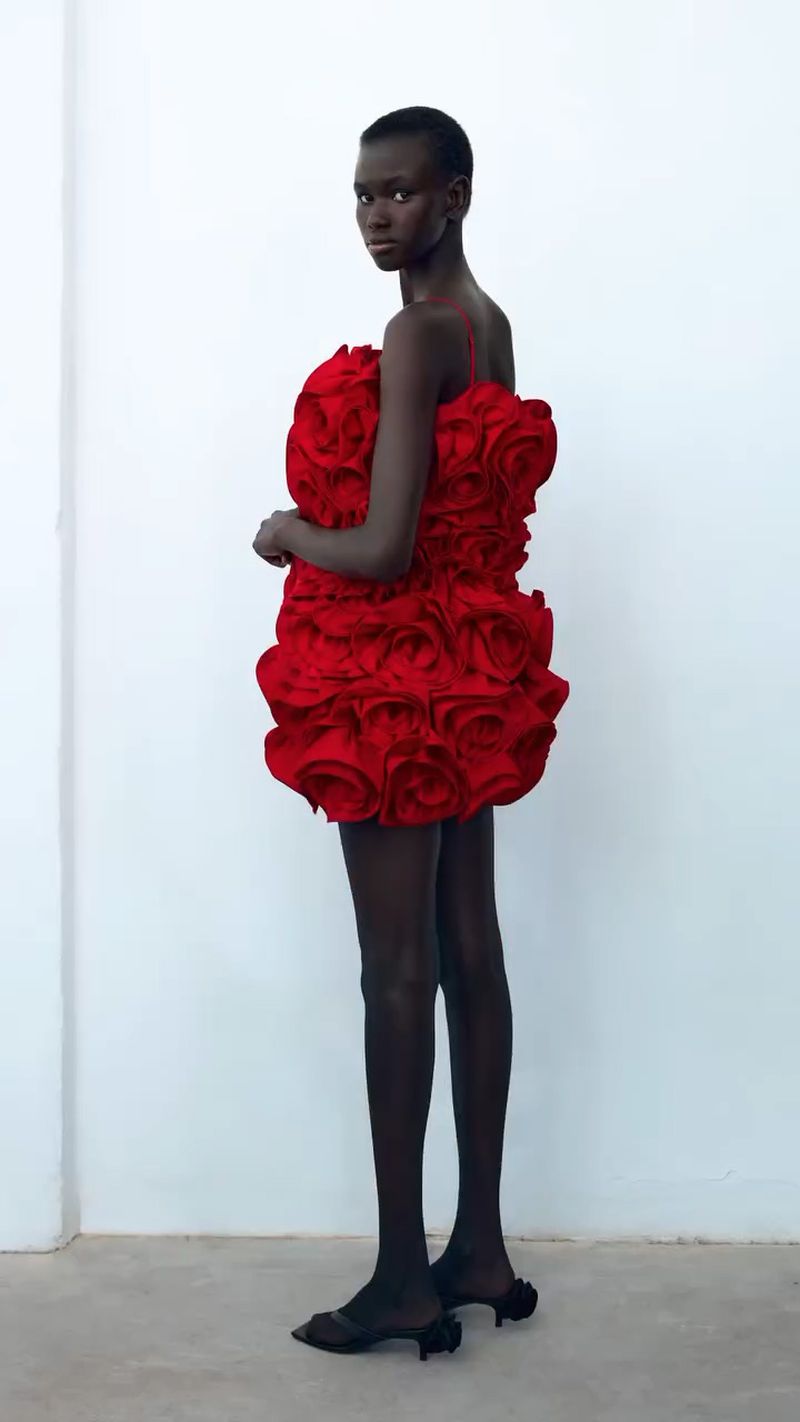 Model in a red rose-textured dress, full shot against a white backdrop, studio lighting, fashion editorial, elegant, and captivating.