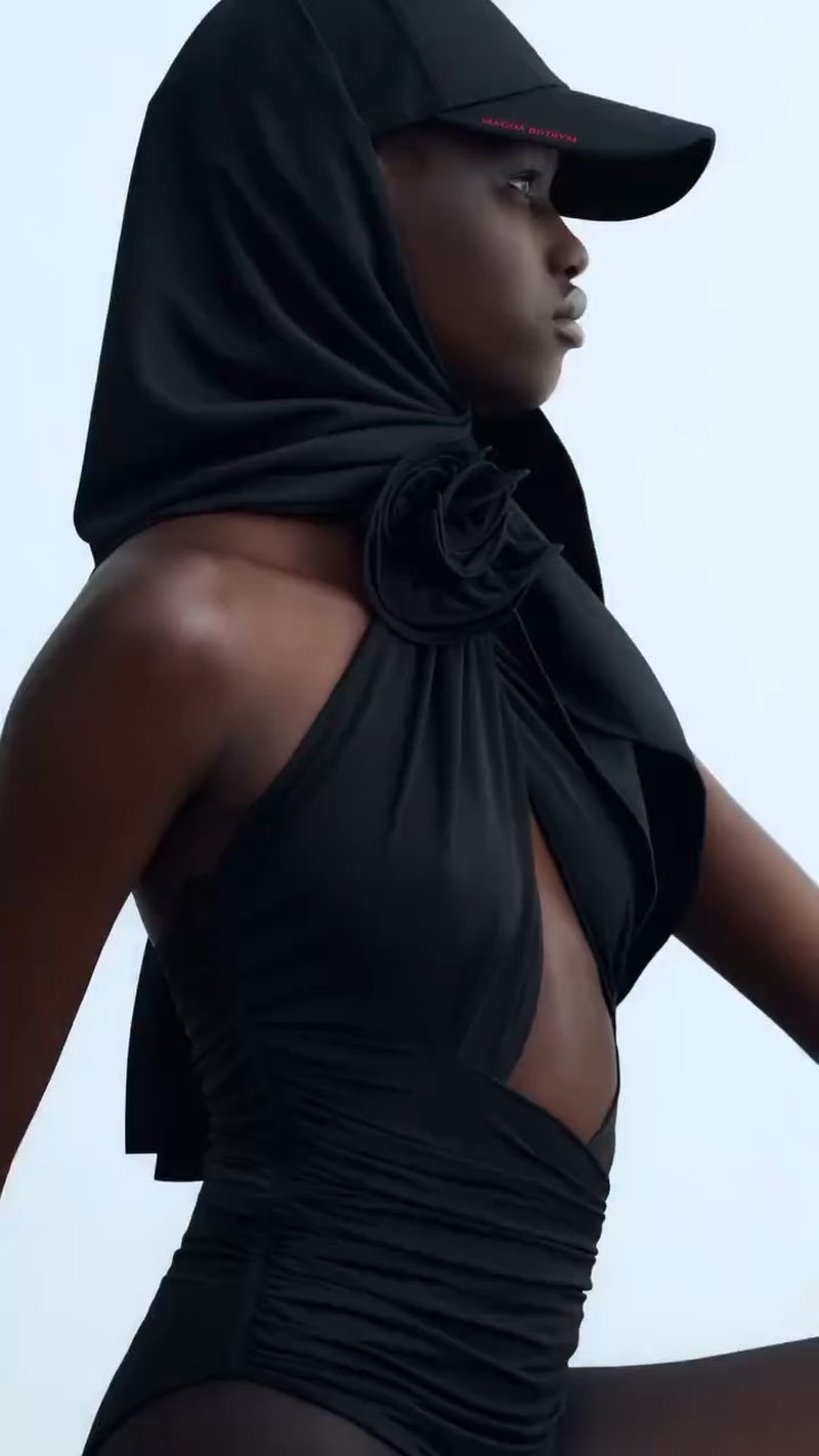 Dark-skinned woman in black swimsuit and baseball cap with black scarf. Beauty and fashion photography, studio lighting, and white background.