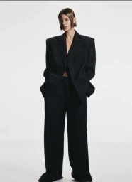 Model wearing an oversized black tailored suit jacket and matching trousers against a plain white studio background.