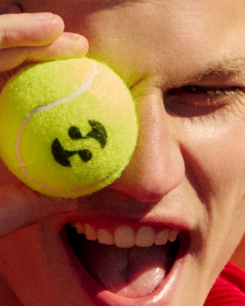Close-up of an adult with an open mouth, holding a tennis ball to their eye in a close-up shot, creating a playful and engaging visual.