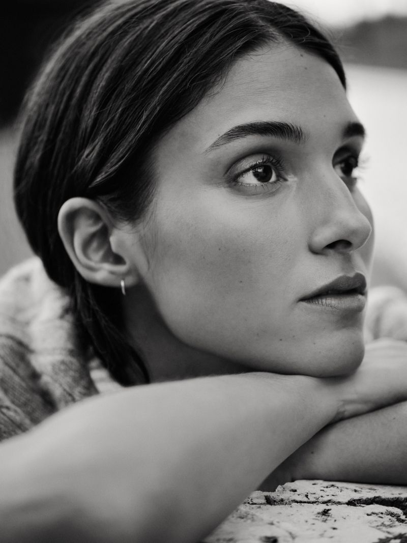 Monochrome portrait of a woman with her head resting on her arms, looking thoughtfully to the right with soft, diffused lighting.