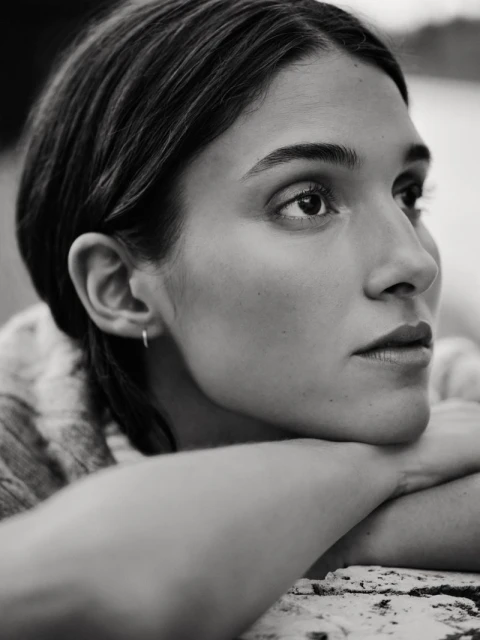 Monochrome portrait of a woman with her head resting on her arms, looking thoughtfully to the right with soft, diffused lighting.