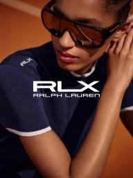 Model wearing dark wrap-around sunglasses and a navy blue top on a tennis court for Ralph Lauren RLX Spring 2025.