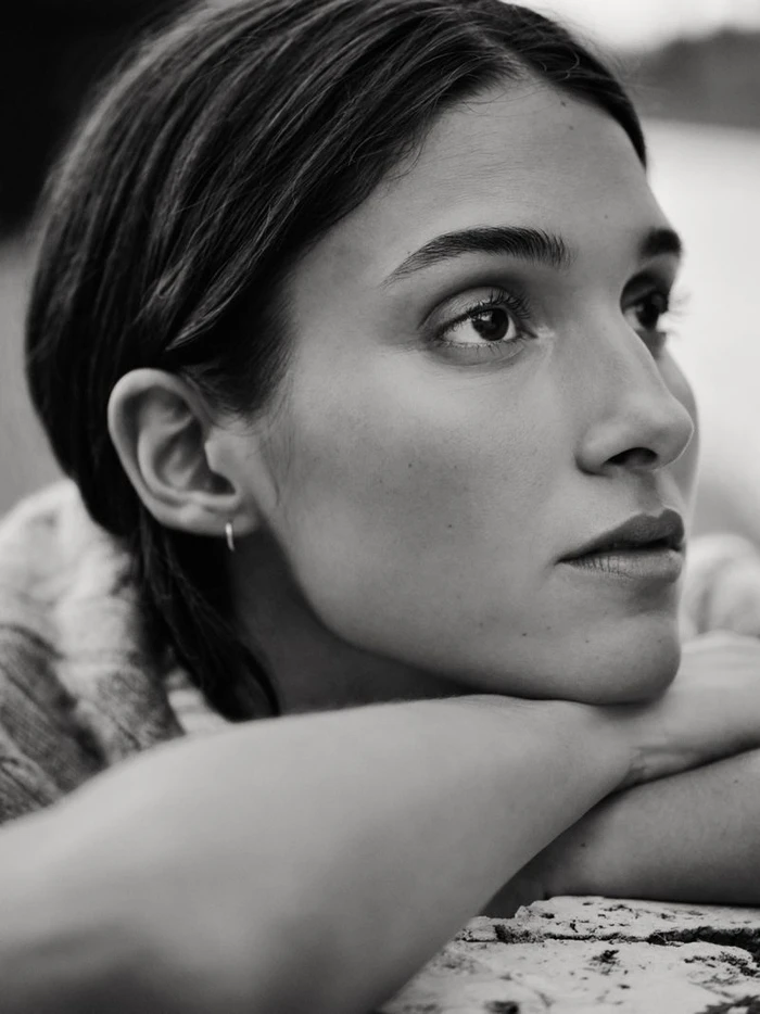 Close up monochrome portrait of a model resting chin on crossed arms outdoors.
