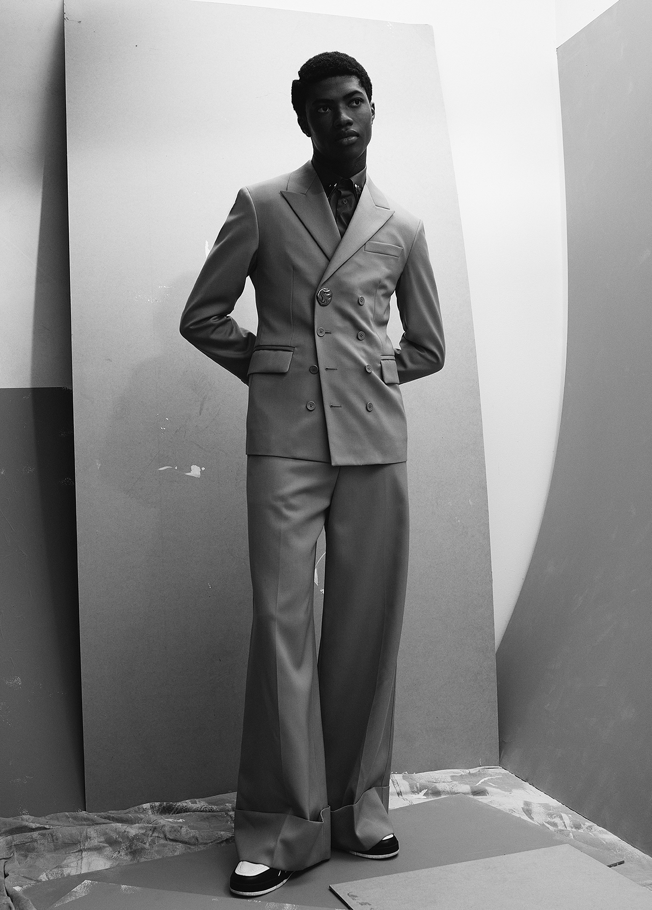 Monochrome portrait of a Black male model in a double-breasted suit with wide-legged trousers, standing indoors in a studio setting.