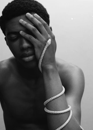 Black man holding hand to forehead with a coiled silver snake bracelet wrapped around his arm