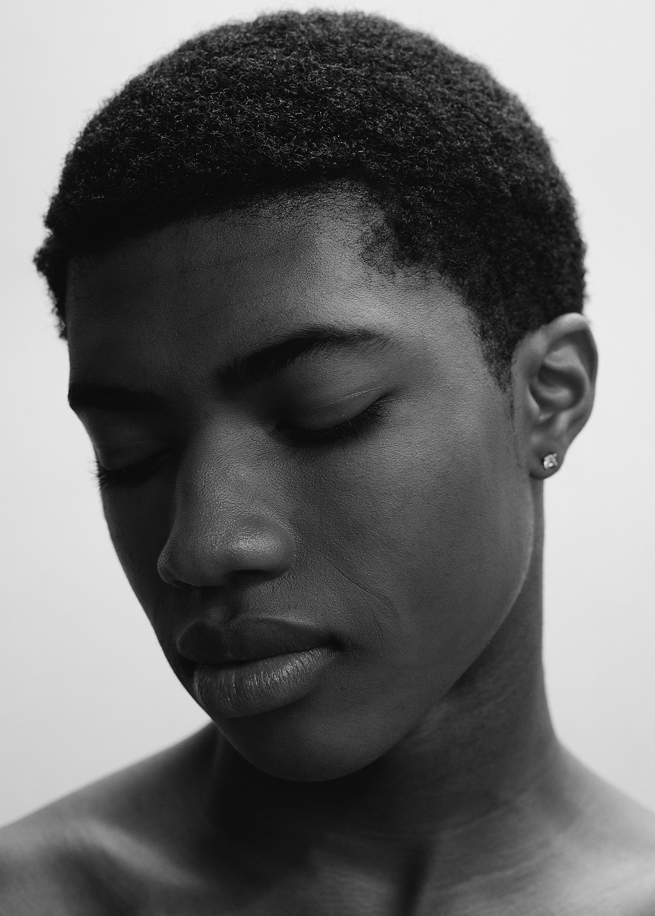 Close-up portrait of a young Black man with eyes closed against a neutral white background