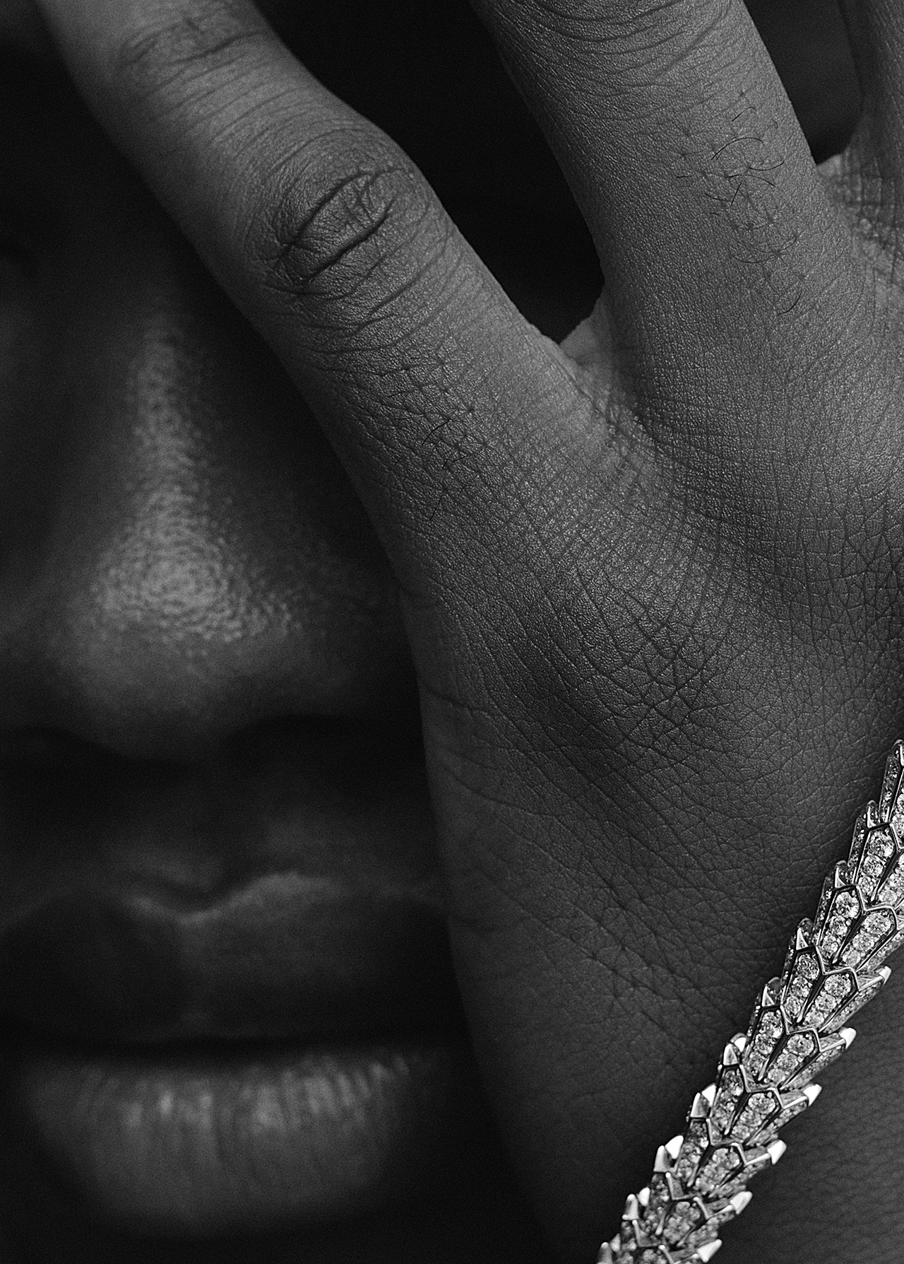 Close-up shot of dark-skinned person's face partially covered by their hand, accentuated with a detailed, decorative bracelet.