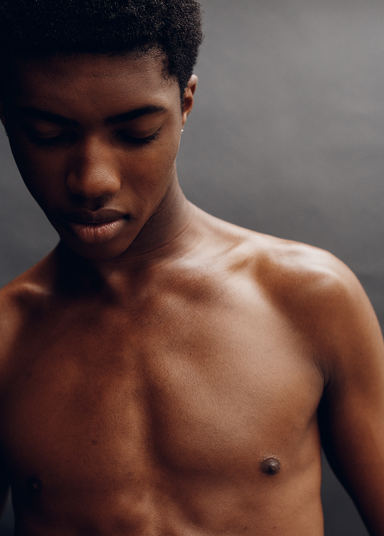Portrait of a shirtless black man looking down against a grey studio backdrop