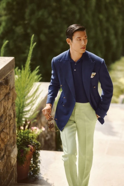A stylish Asian man walks down steps wearing a blazer, polo shirt, and slacks, accessorized with sunglasses. The scene is outdoors.
