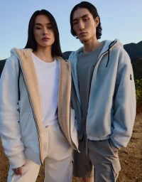 Two models standing outdoors wearing casual fleece zip hoodies and t-shirts against a mountain backdrop for Moose Knuckles