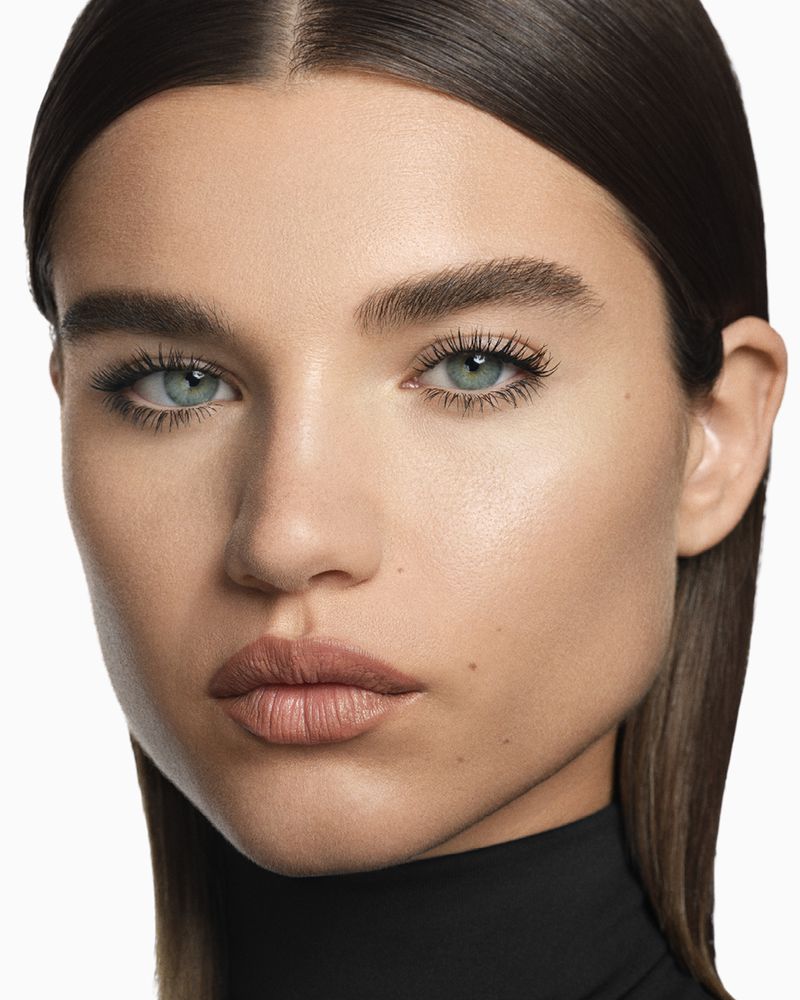 Close-up portrait of a fair-skinned woman with light brown hair, light eyes, and natural makeup, wearing a black top against a white background.