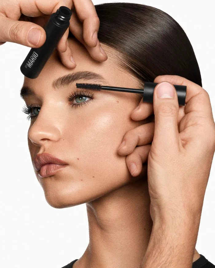 Close-up portrait of model Meghan Roche having black mascara applied by a makeup artist for Makeup by Mario.
