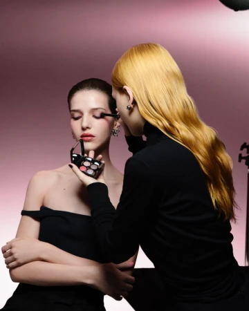 Model getting makeup applied by makeup artist with pink backdrop in studio setting with studio lighting. Beauty and cosmetics concept.