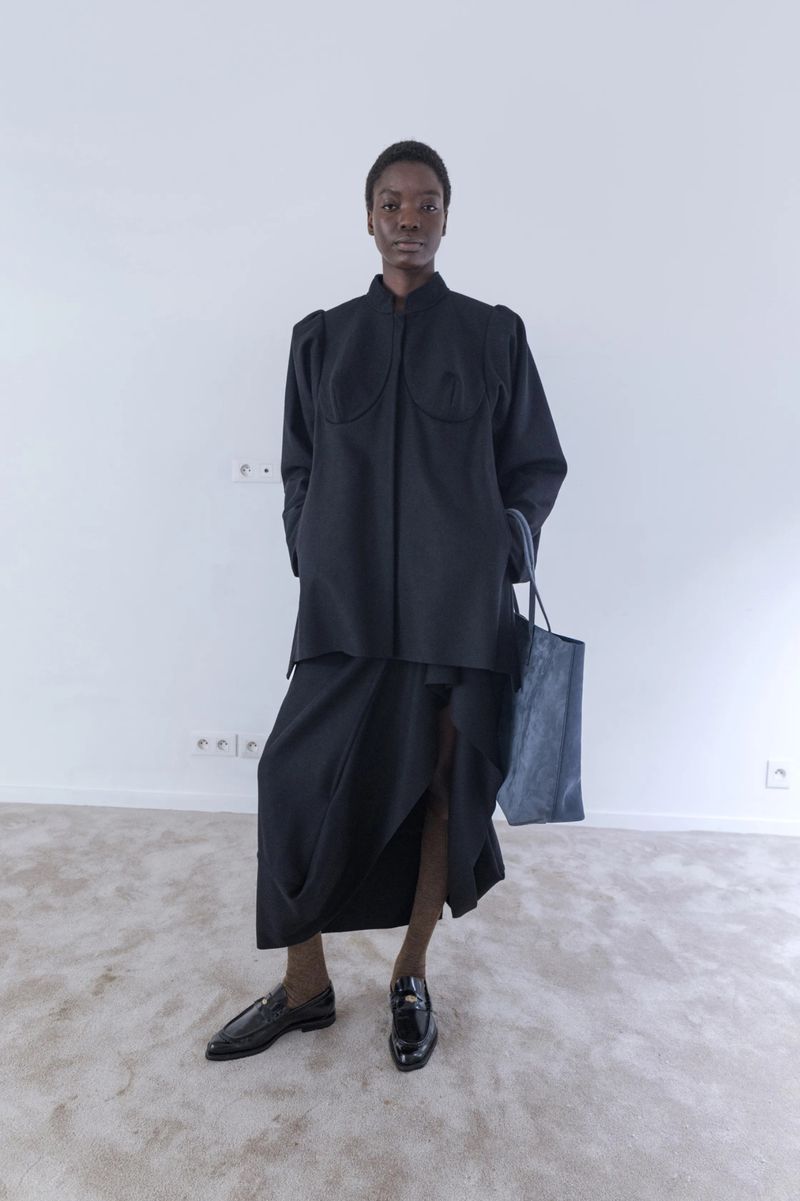 Model wearing black jacket and skirt holding a tote bag in a room photographed by Pavel Golik for Vivienne Westwood