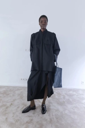 Model wearing black jacket and skirt holding a tote bag in a room photographed by Pavel Golik for Vivienne Westwood