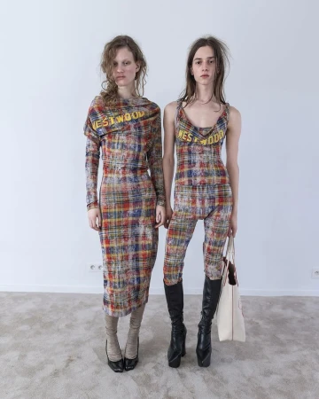 Two models standing in plaid Vivienne Westwood outfits against a plain wall and neutral carpet floor