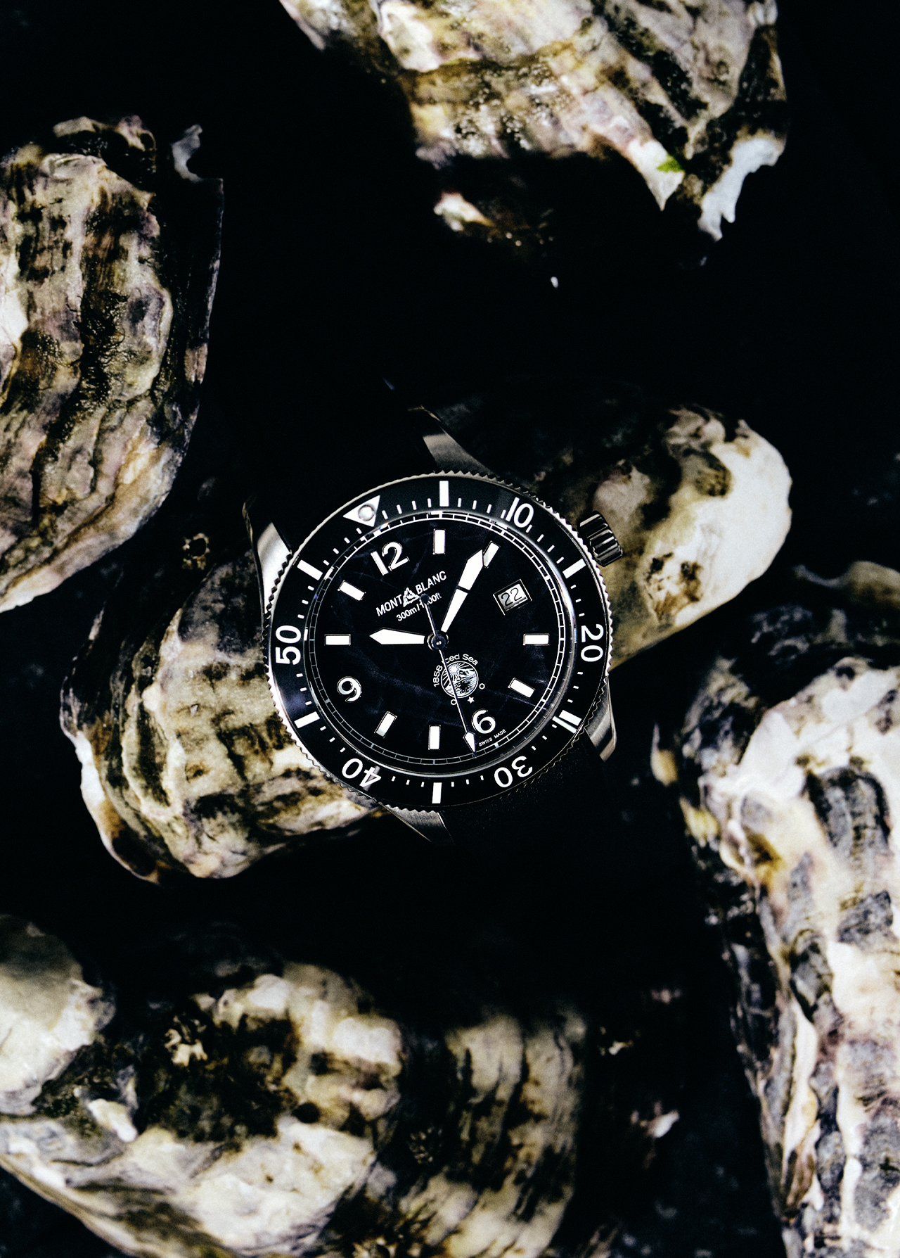 Montblanc watch on a bed of oyster shells with a black dial, silver casing, and clear numerals, offering a luxurious and nautical aesthetic.