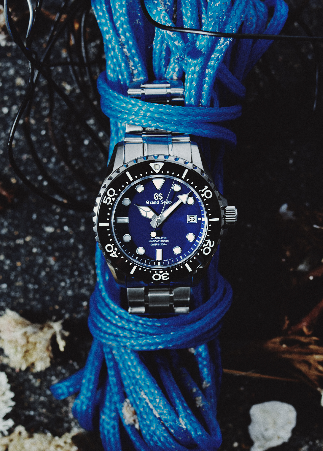 Luxury wristwatch on blue rope with blurred rock surface background, studio shot. Ideal for horology enthusiasts and accessory promotion.