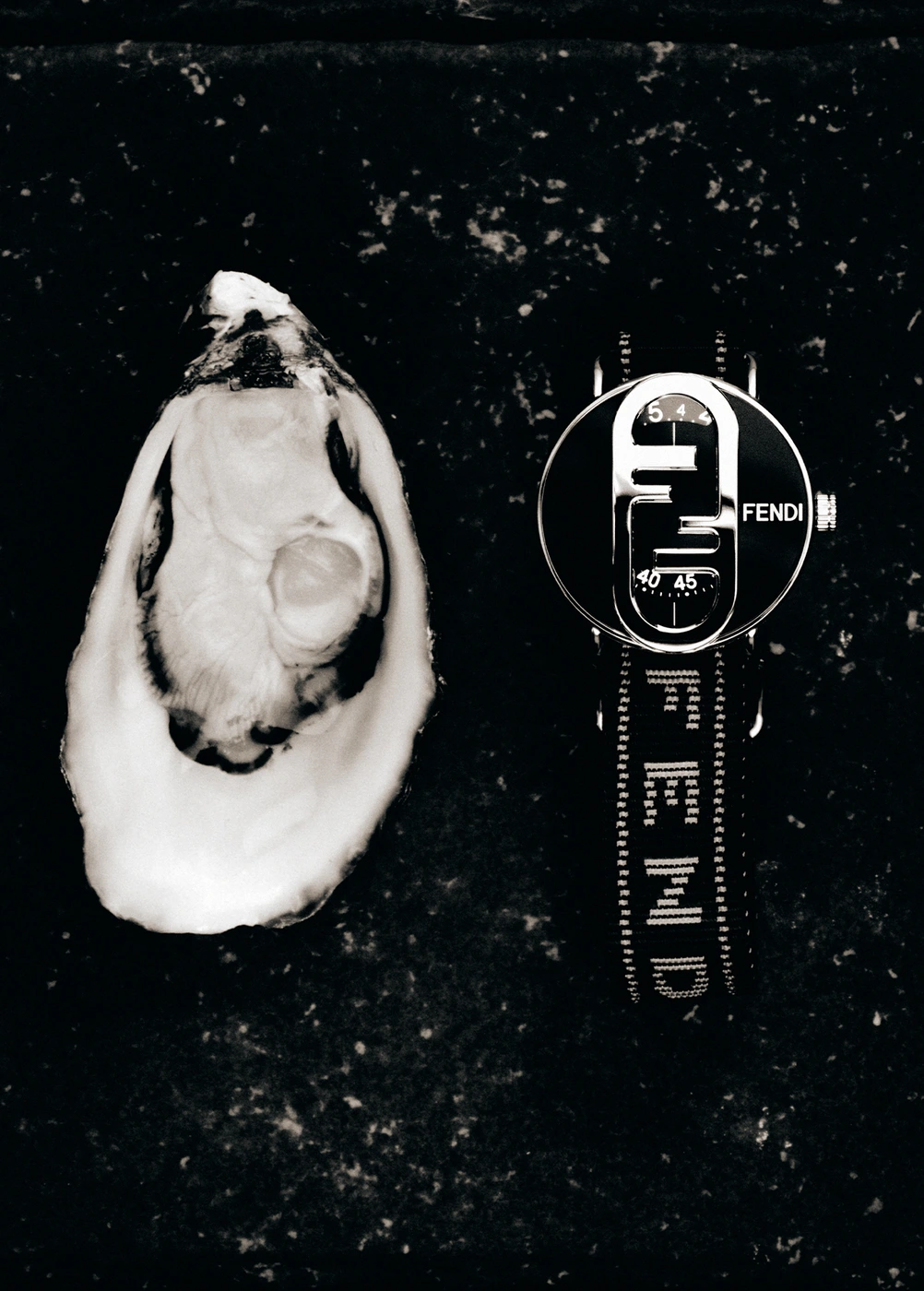 An open oyster placed beside a luxury designer wristwatch on a dark textured surface.
