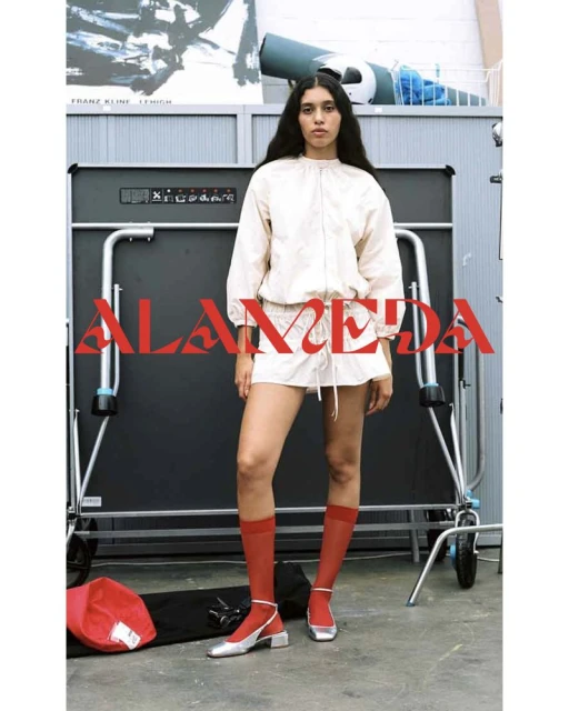 Fashionable woman in a neutral outfit, red socks, and silver shoes posing near a ping pong table and equipment for a fashion shoot.