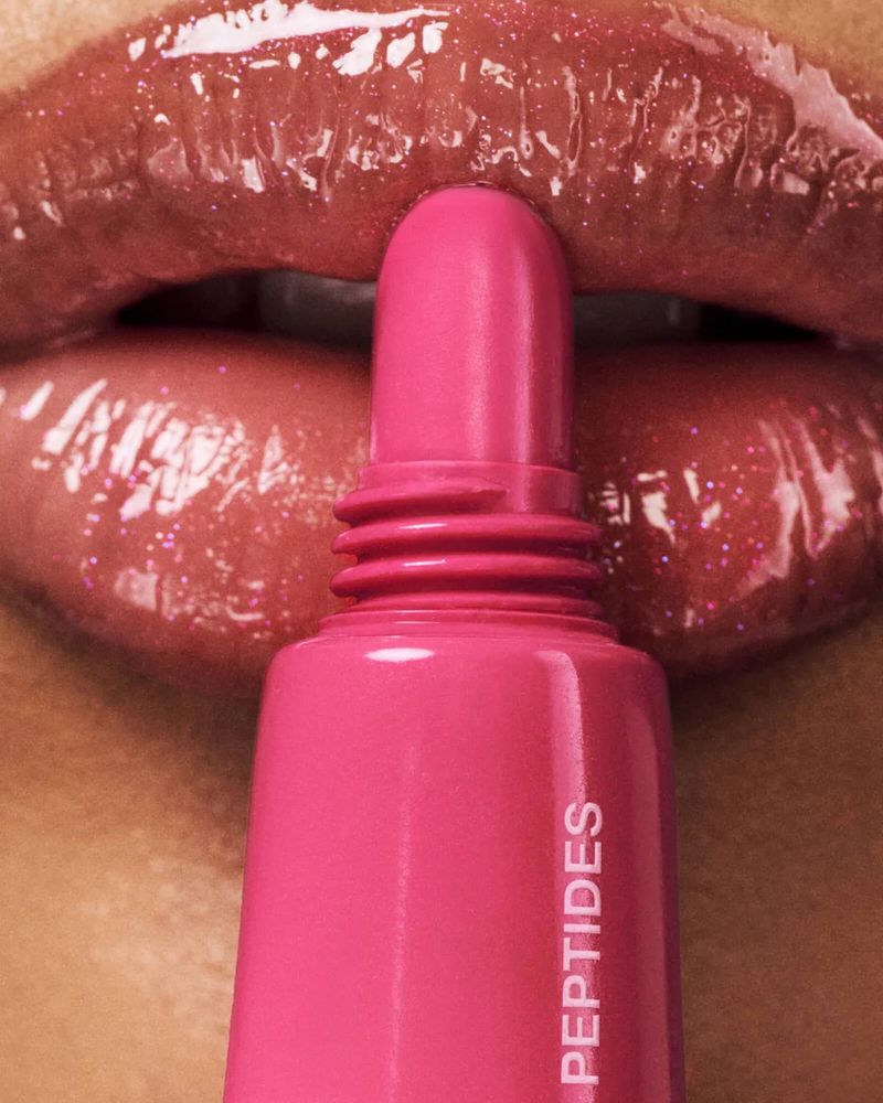 Close-up of a woman's shiny lips with pink lip gloss tube. Cosmetics shot highlighting texture, color, and application.